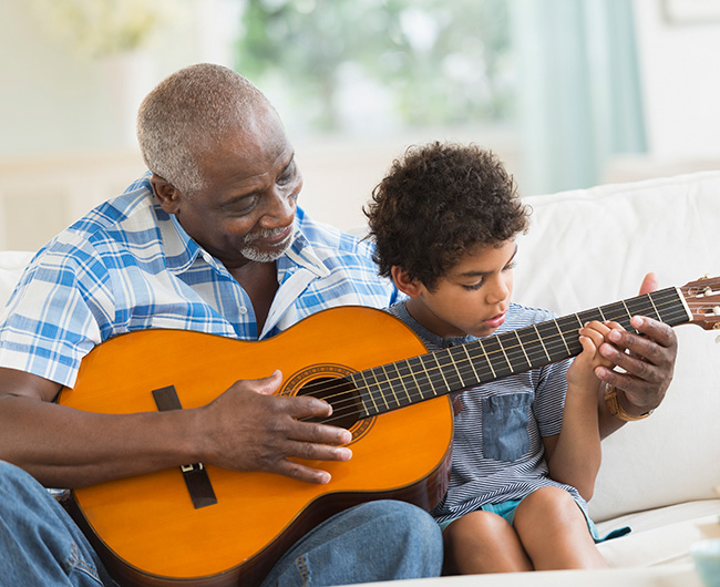 Elderly man showing grandson how to play guitar